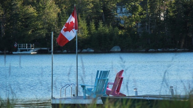 Canadian flag on jetty with adirondack chairs in lake