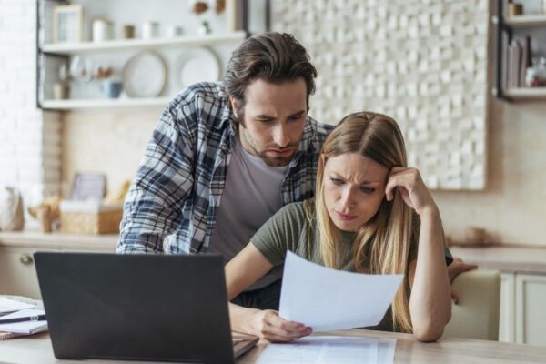 Unhappy young caucasian family think look at document pay bills and taxes at table with laptop