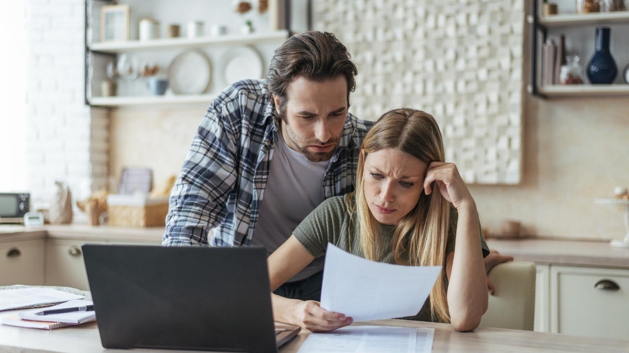 Unhappy young caucasian family think look at document pay bills and taxes at table with laptop