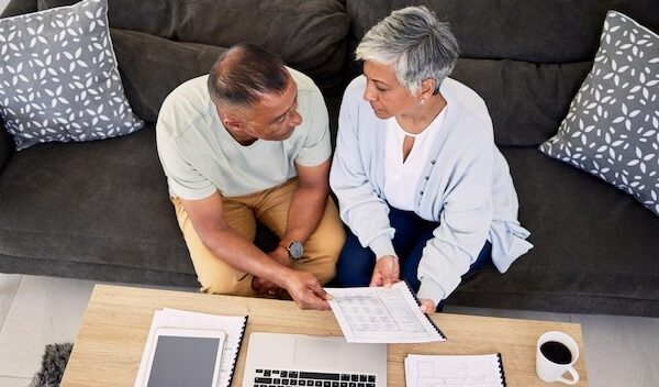 Senior couple tax documents and laptop in home living room for discussion planning and finance Elderly man old woman and paperwork for financial compliance in top view lounge sofa and retirement