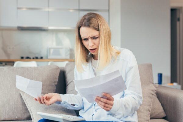 Worried housewife pays inflated bills while sitting on sofa at home, frustrated with work, and monthly income