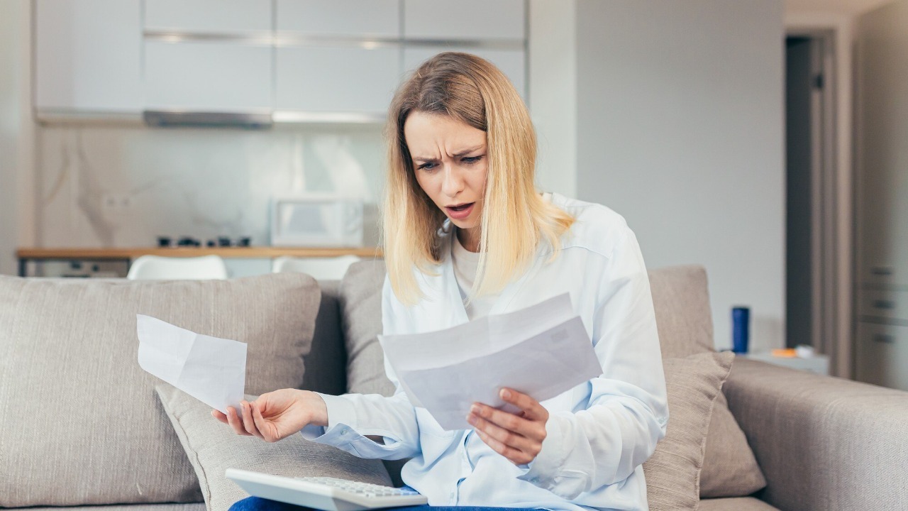 Worried housewife pays inflated bills while sitting on sofa at home, frustrated with work, and monthly income