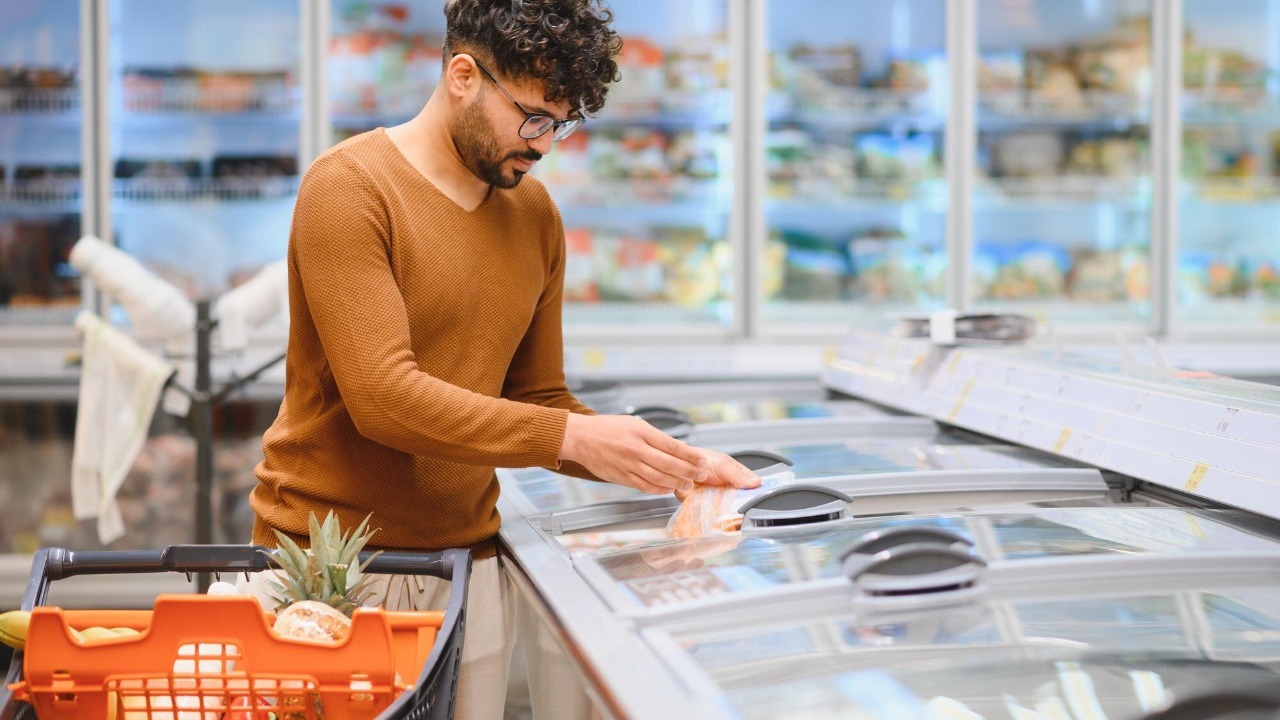 Arab customer choosing frozen food in supermarket refrigerator