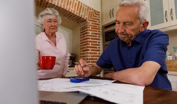 Senior caucasian couple spending time at home together, sitting in kitchen, the man looking at paperwork and the woman holding a cup. isolating during coronavirus covid 19 quarantine lockdown.
