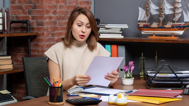 Front view of wondered woman checking papers sitting at office