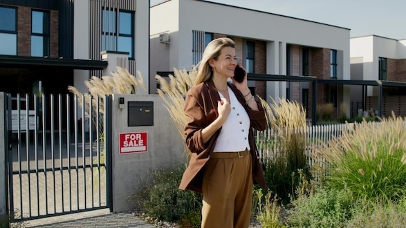 A woman is talking on her mobile phone near a house for sale