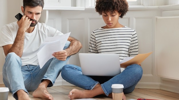Photo of two mixed race coworkers read documentation, concentrated on solving problem with planning