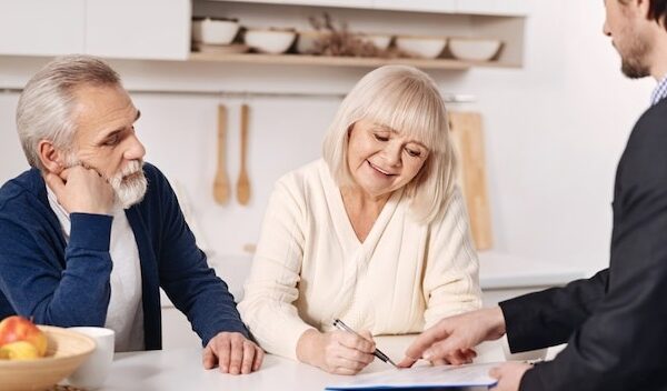 The moment of signing the agreement. Decisive positive senior couple sitting at home and having conversation with social security advisor while signing the agreement