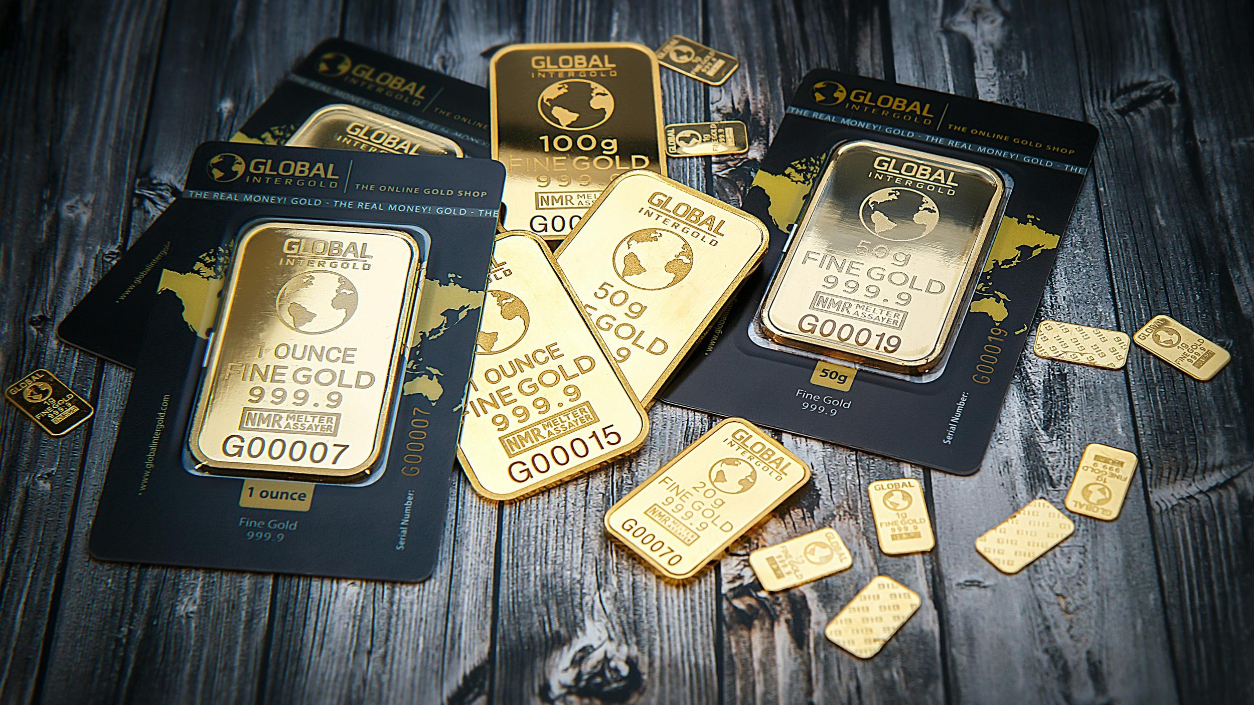 A collection of fine gold bars displayed on a textured wooden surface.