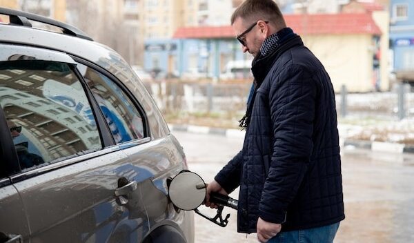 A man with a blue jacket and dark glasses at a gas station He fills up the car Petrol Lifestile