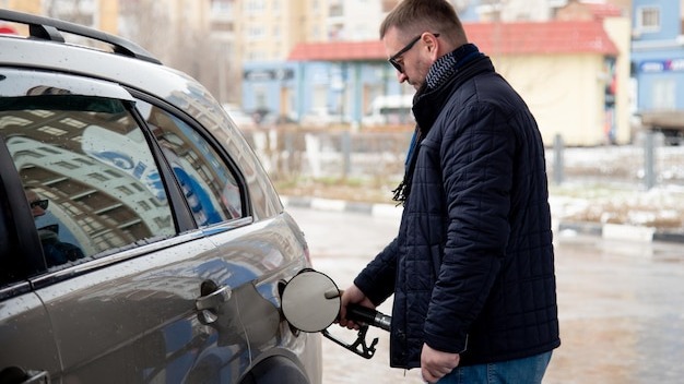 A man with a blue jacket and dark glasses at a gas station He fills up the car Petrol Lifestile
