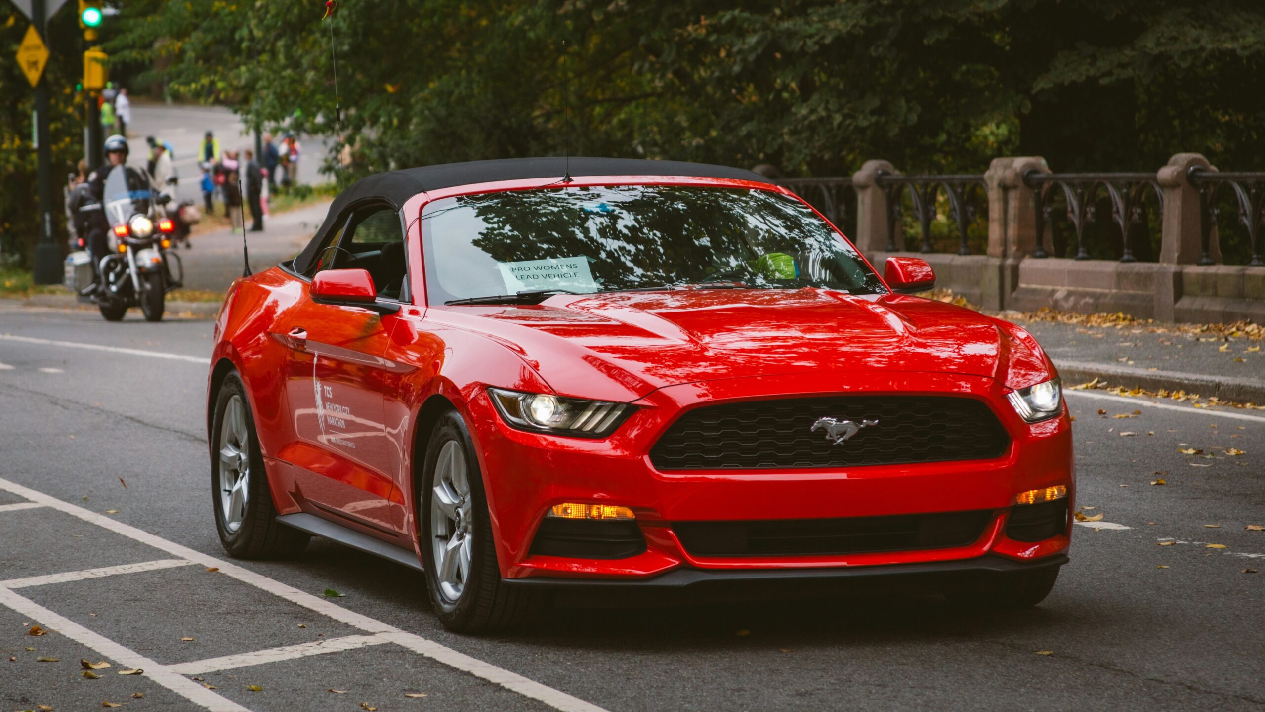 A red convertible mustang is driving down the street.