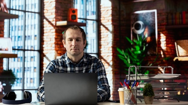 Man seated at home office desk using laptop checking emails displayed on screen