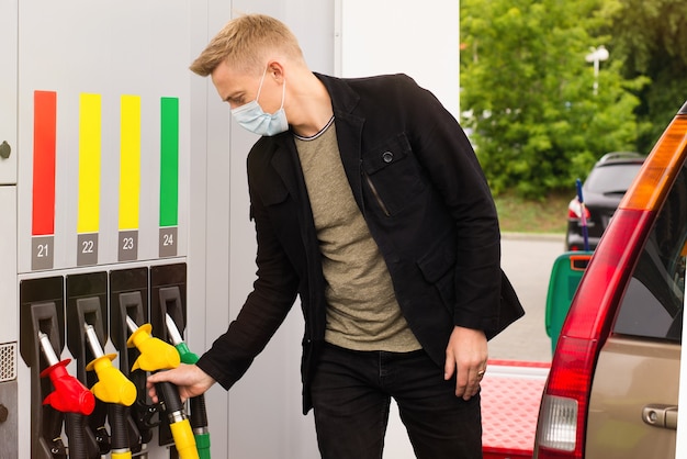 a young man in a disposable mask refuels a car at a gas station