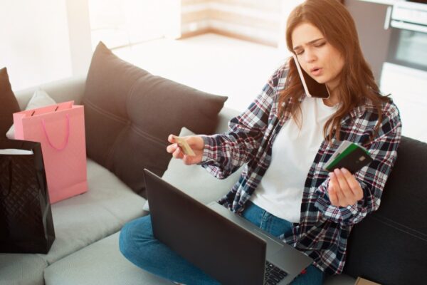 Online shopping. A young woman sits on a couch and dictates her credit card details to a seller in an online store.