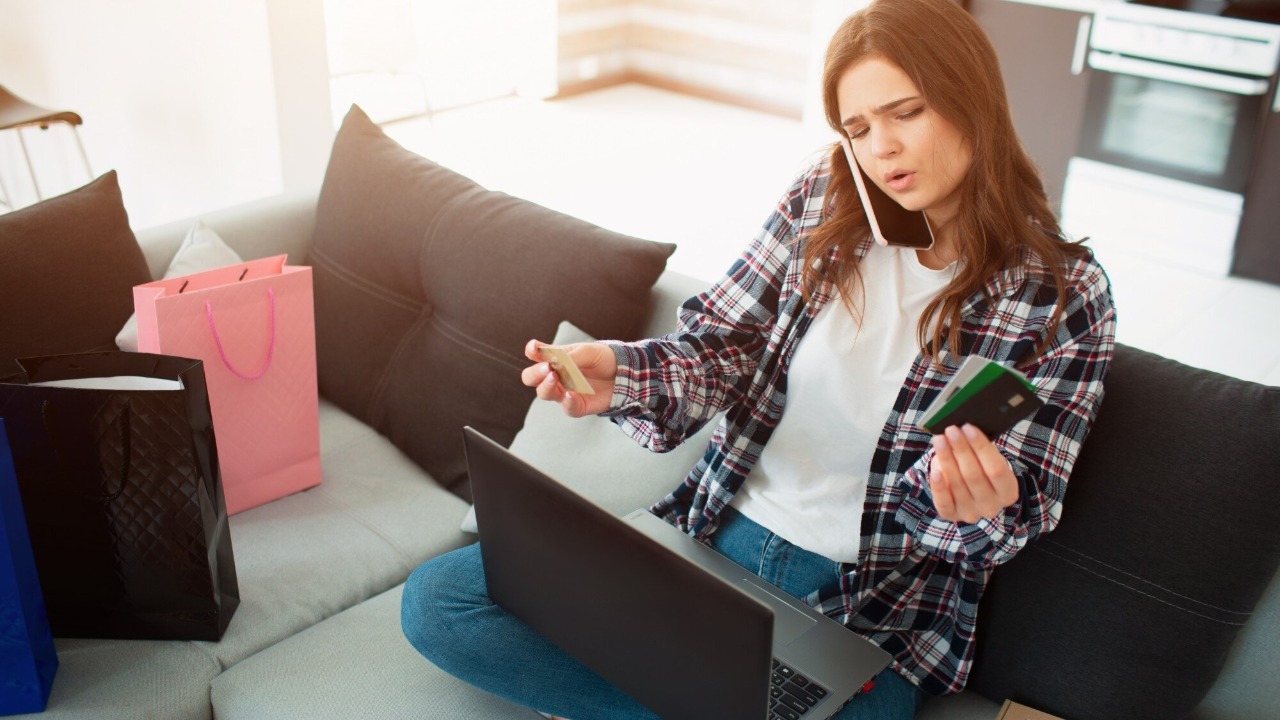 Online shopping. A young woman sits on a couch and dictates her credit card details to a seller in an online store.