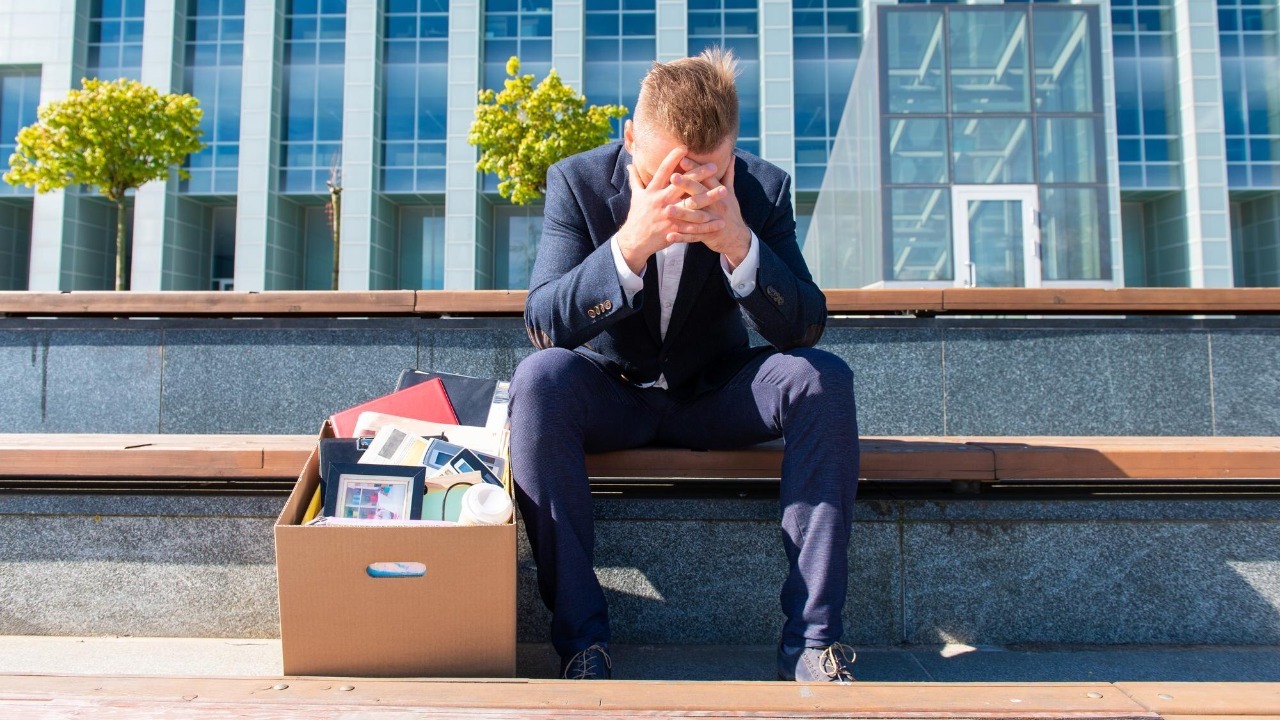 Stress and jobless concept, former employee sitting with his belongings stuffed in a box next to him