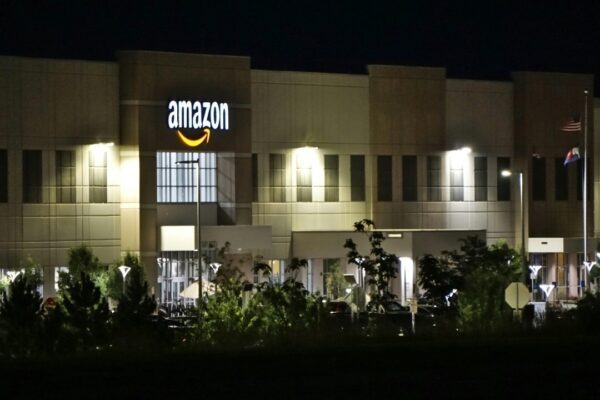 Amazon warehouse building illuminated at night with trees and signage.
