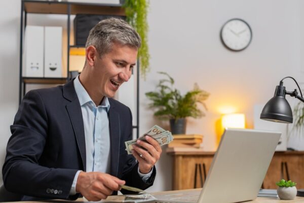 Caucasian young businessman in suit working on laptop pc counting money cash at home office desk