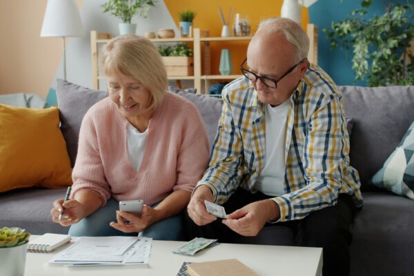 Elderly couple reviews finances at home on couch.