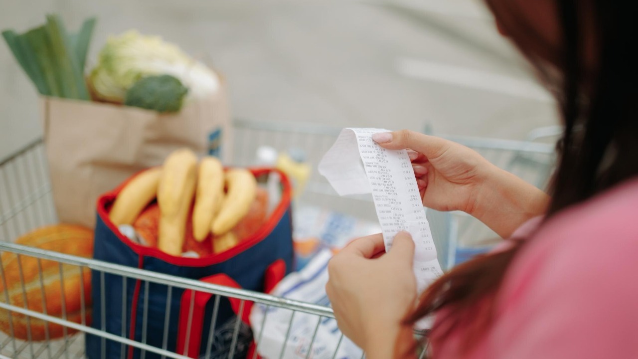 Woman hands holding receipt with a full shopping cart in view