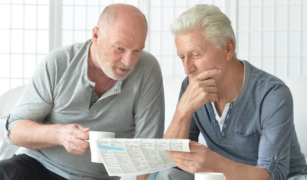 Two senior men sitting at table and reading newspaper