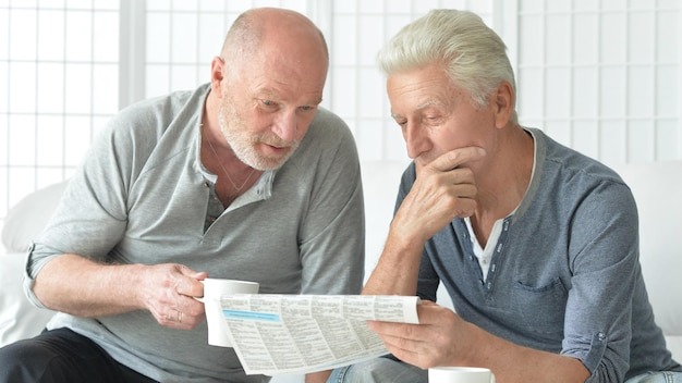 Two senior men sitting at table and reading newspaper