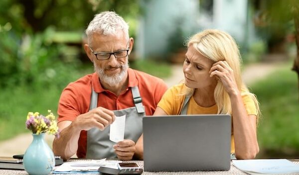 Stressed senior couple with laptop checking bills sitting at table in garden