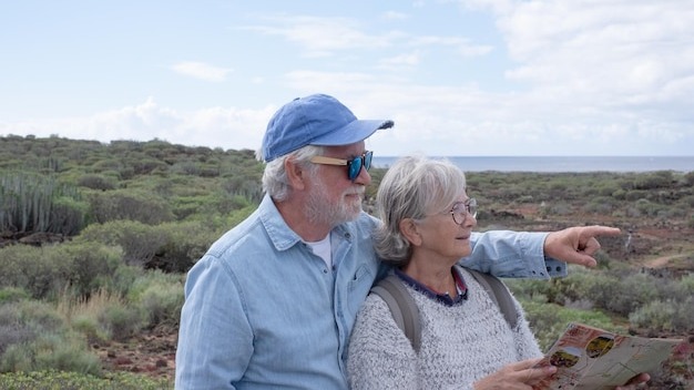 Carefree senior couple in walking day in countryside looking at footpath map enjoying trekking day