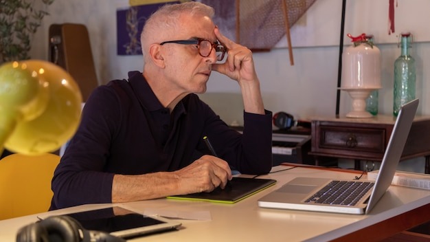 Middle aged man using computer in his art studio and drawing on his tablet