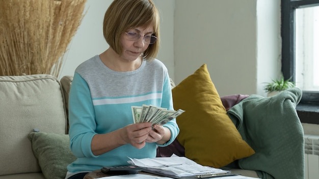 Senior mature woman using calculator holding paper bill calculating money budget tax