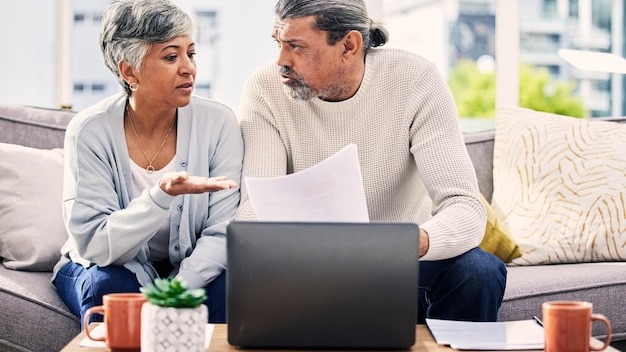 Senior couple documents and stress on laptop with financial paperwork taxes or retirement questions at home Planning debt and elderly people on sofa for life insurance bills or asset management