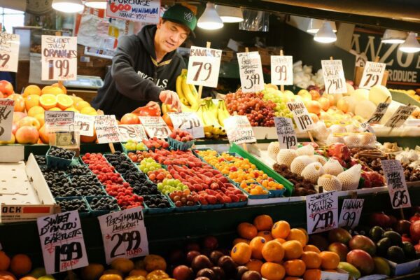 man in black jacket standing in front of fruit stand