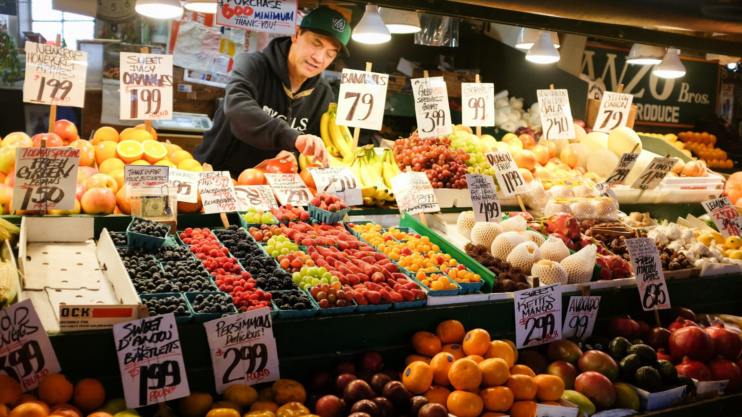 man in black jacket standing in front of fruit stand