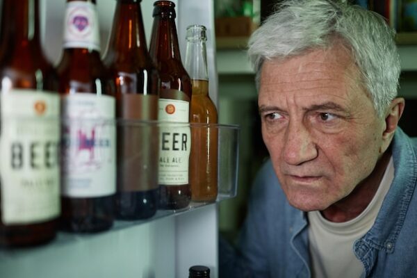 Senior man looking inside refrigerator containing beer bottles