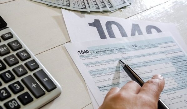 female hand with pen tax forms 1040 and dollars on wood background
