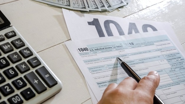 female hand with pen tax forms 1040 and dollars on wood background