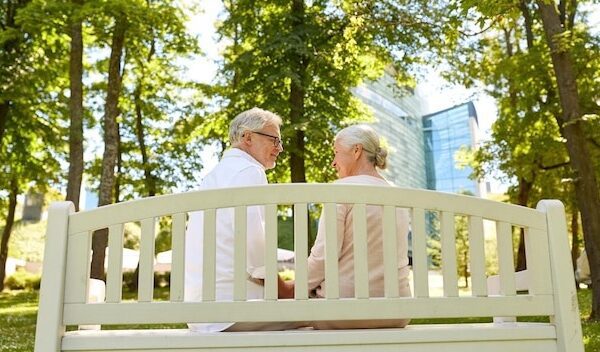 old age, relationship and people concept - happy senior couple sitting on bench at summer city park