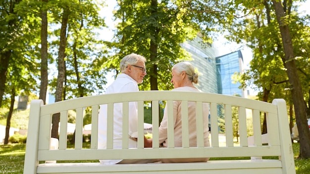 old age, relationship and people concept - happy senior couple sitting on bench at summer city park