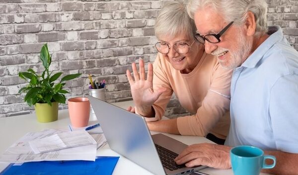 Attractive elderly couple smile while video chat by laptop with family or friends