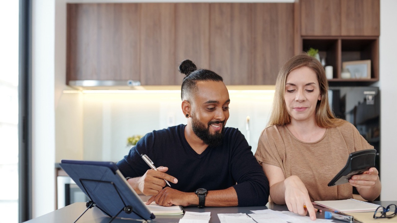 Young couple sitting at kitchen table and checking bills and paychecks and calculating family expences