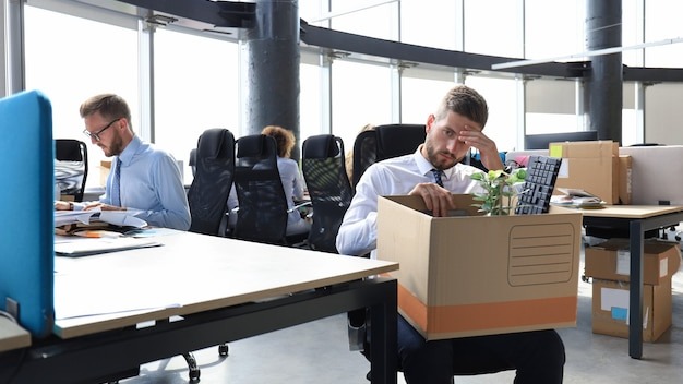 Sad dismissed worker are taking his office supplies with him from office.