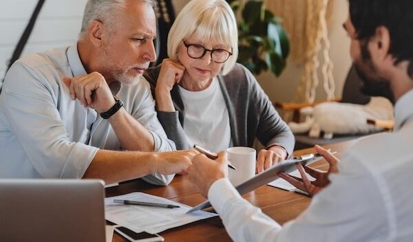 Financial advisor explaining paperwork to elderly retired couple front of desk