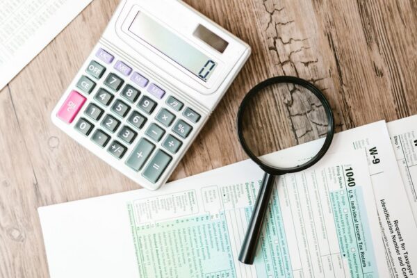 Tax forms, a calculator and a magnifying glass on a wooden table