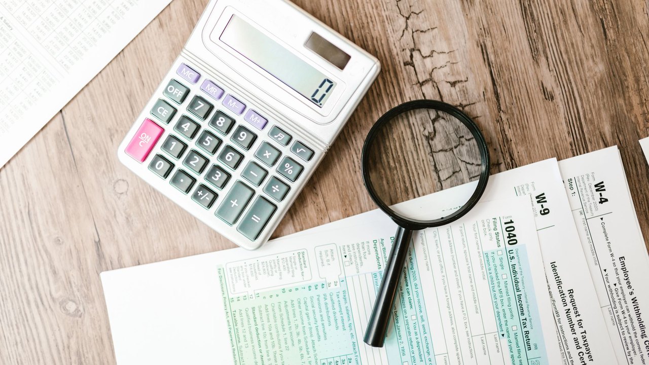 Tax forms, a calculator and a magnifying glass on a wooden table
