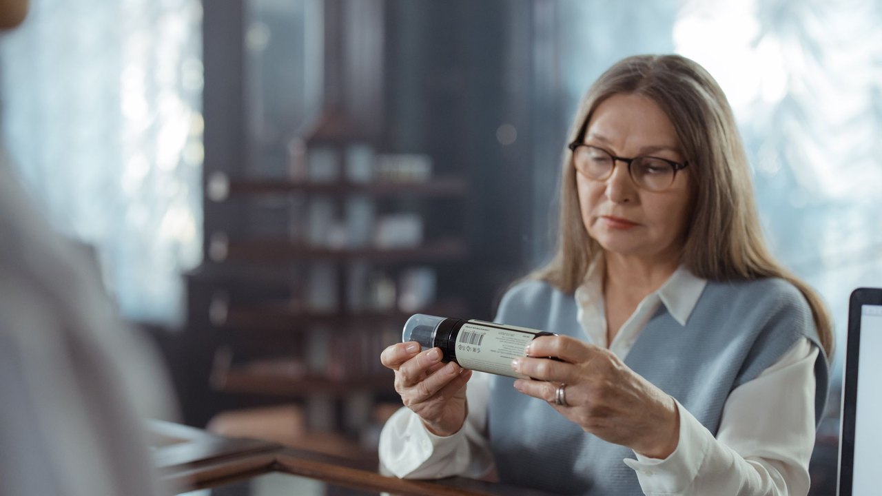 Older woman reading a prescription bottle at a pharmacy counter